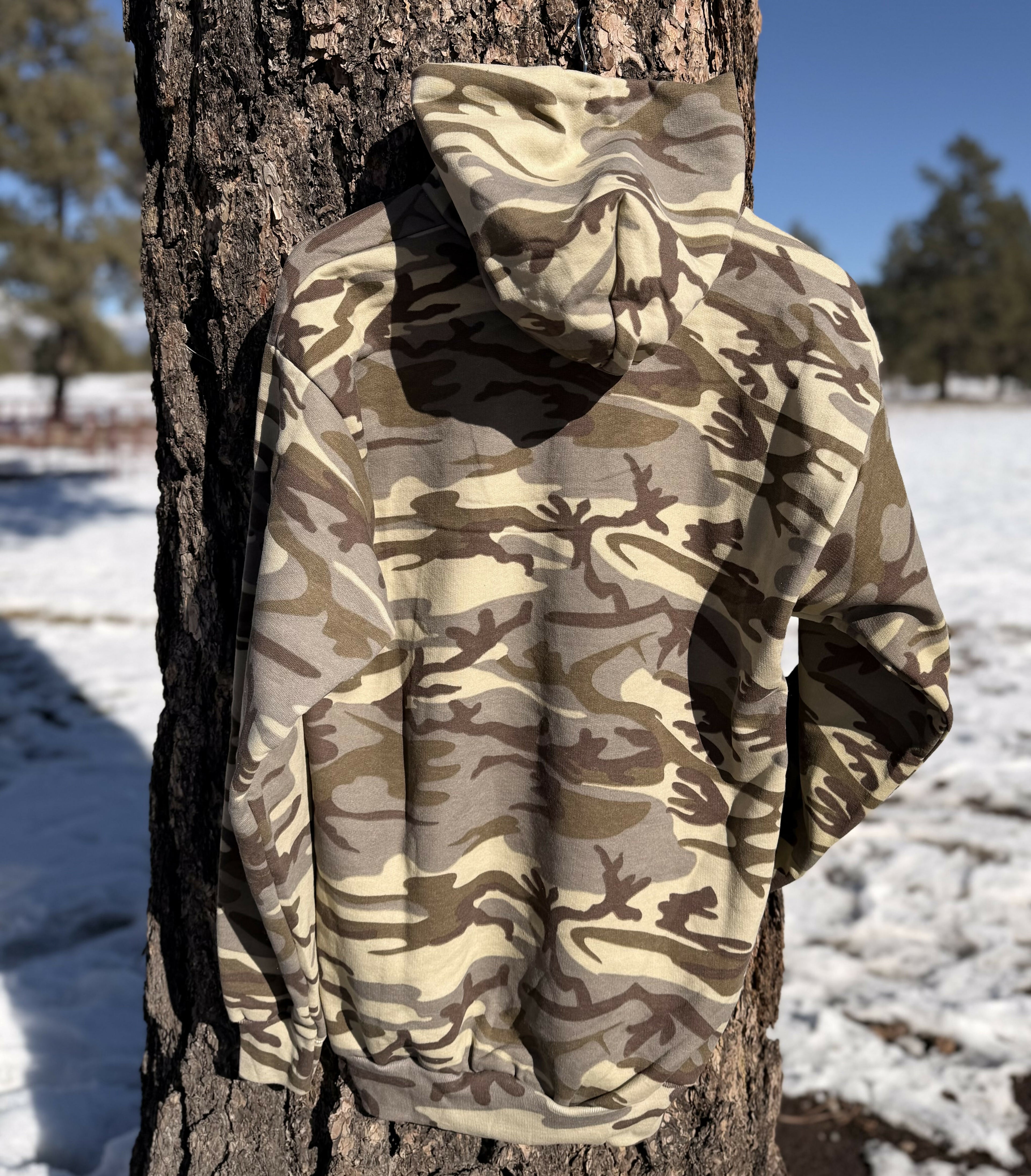 camo hoodie back hanging on a tree outdoors with a woods background