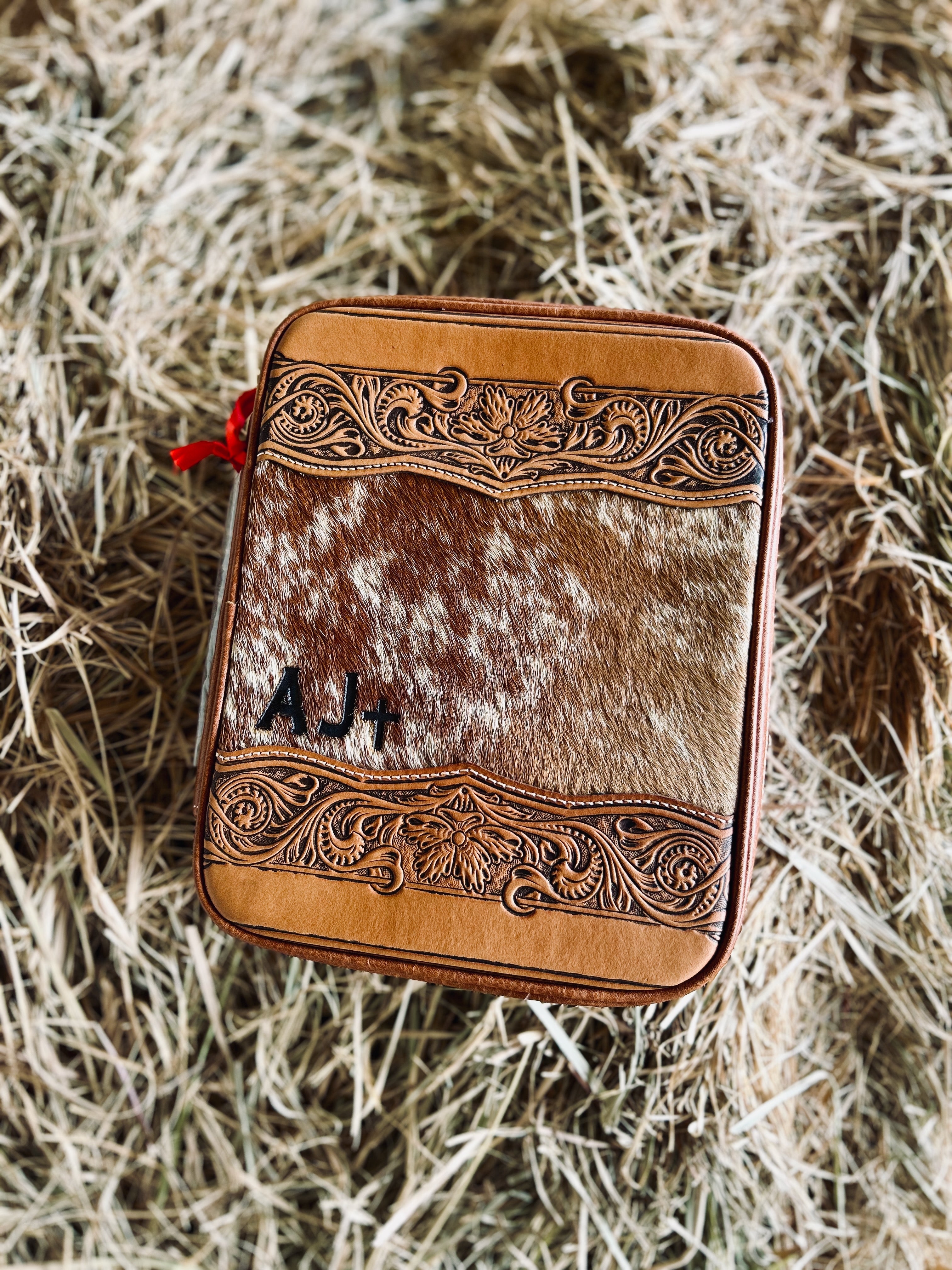 Leather and cowhide wallet with intricate designs on a hay background