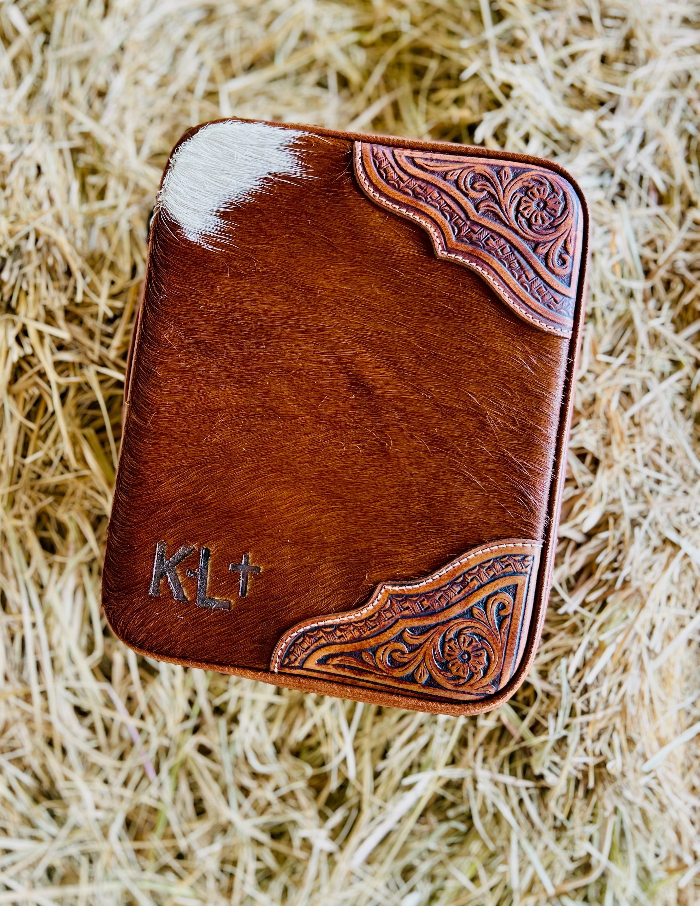 Brown leather wallet with cowhide pattern and 'KL+' monogram on a hay background