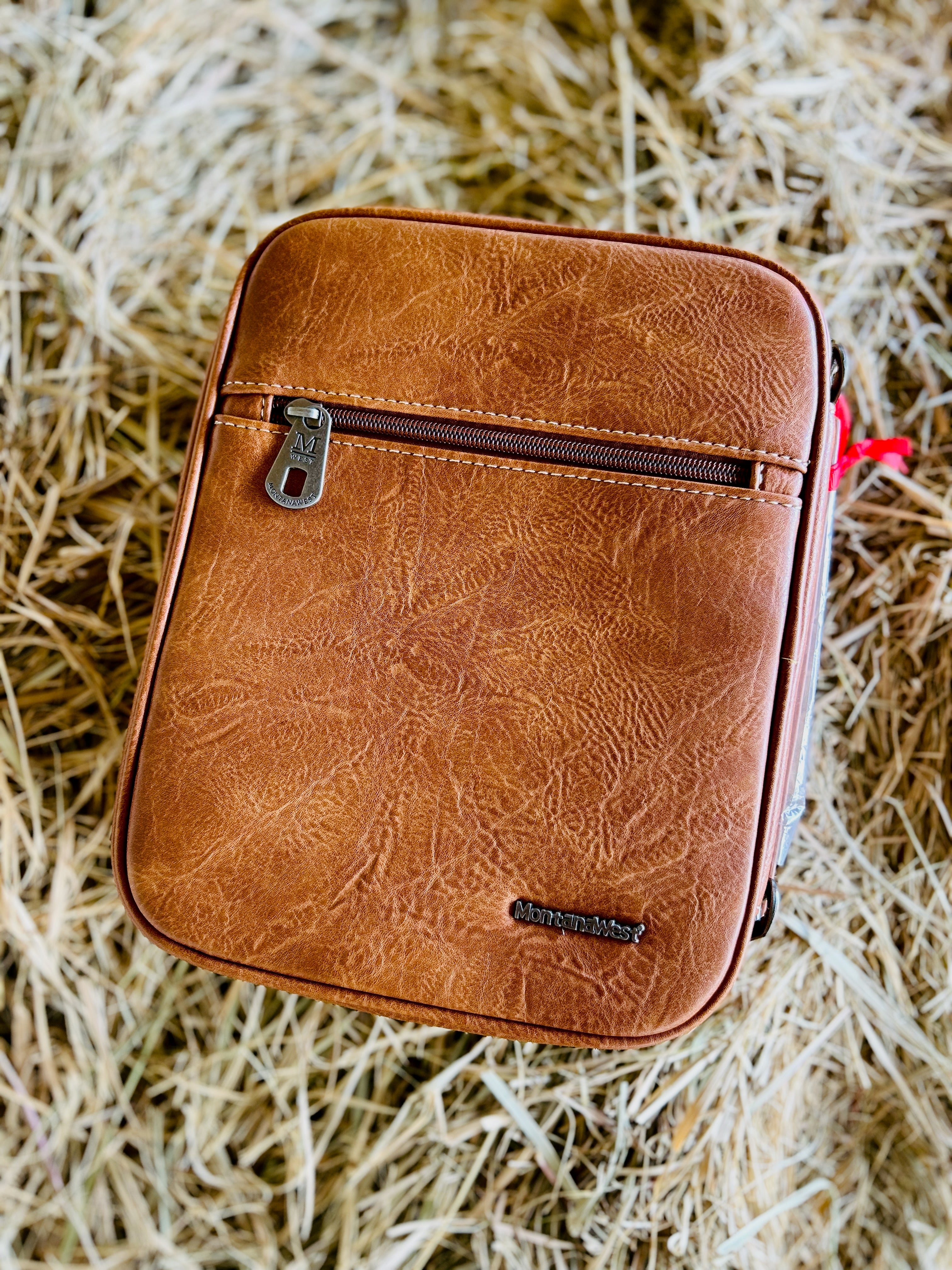 Brown leather pouch with a zipper on a straw background