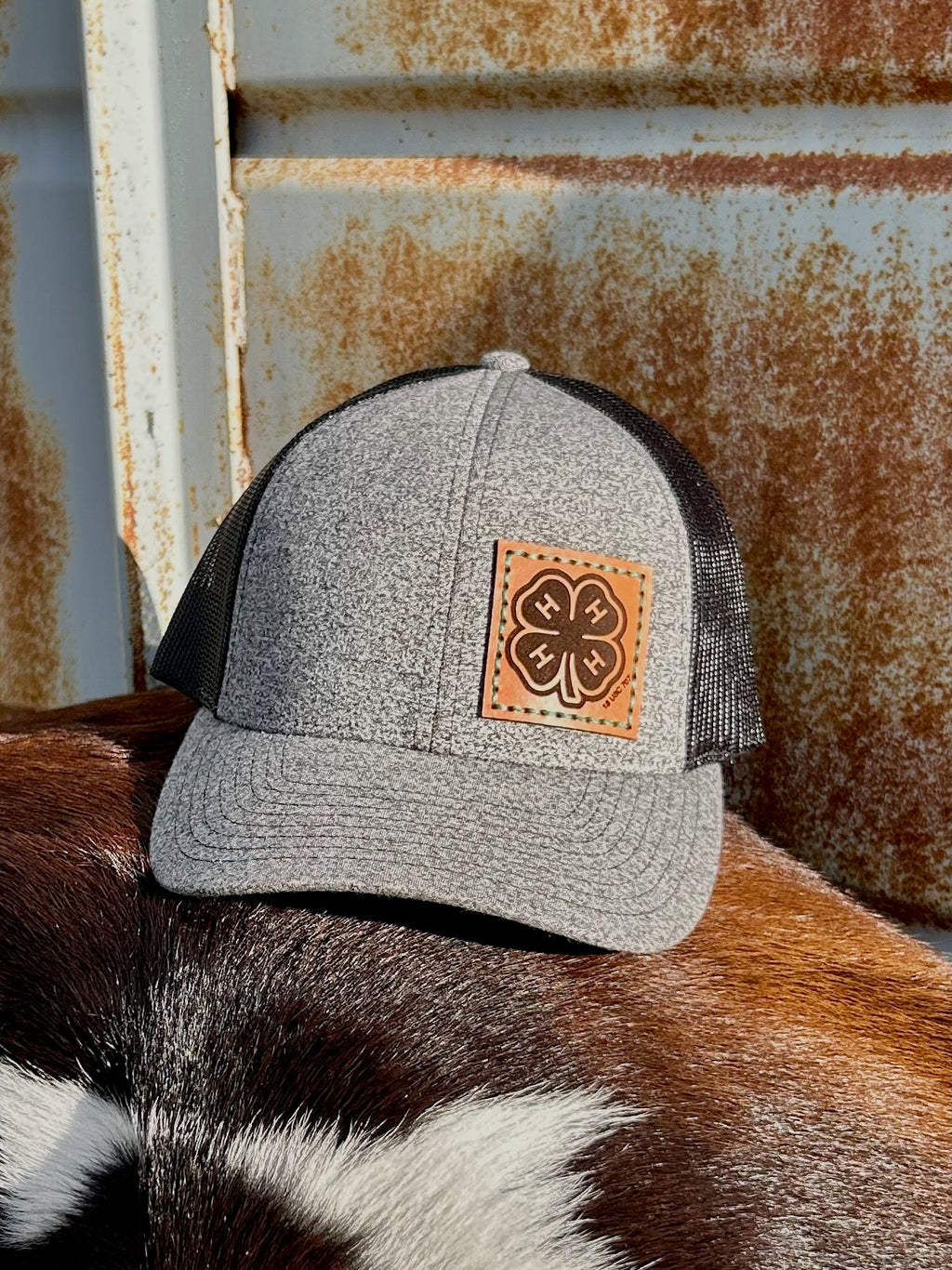 Gray trucker cap with a leather patch on a cowhide surface with rusted metal background