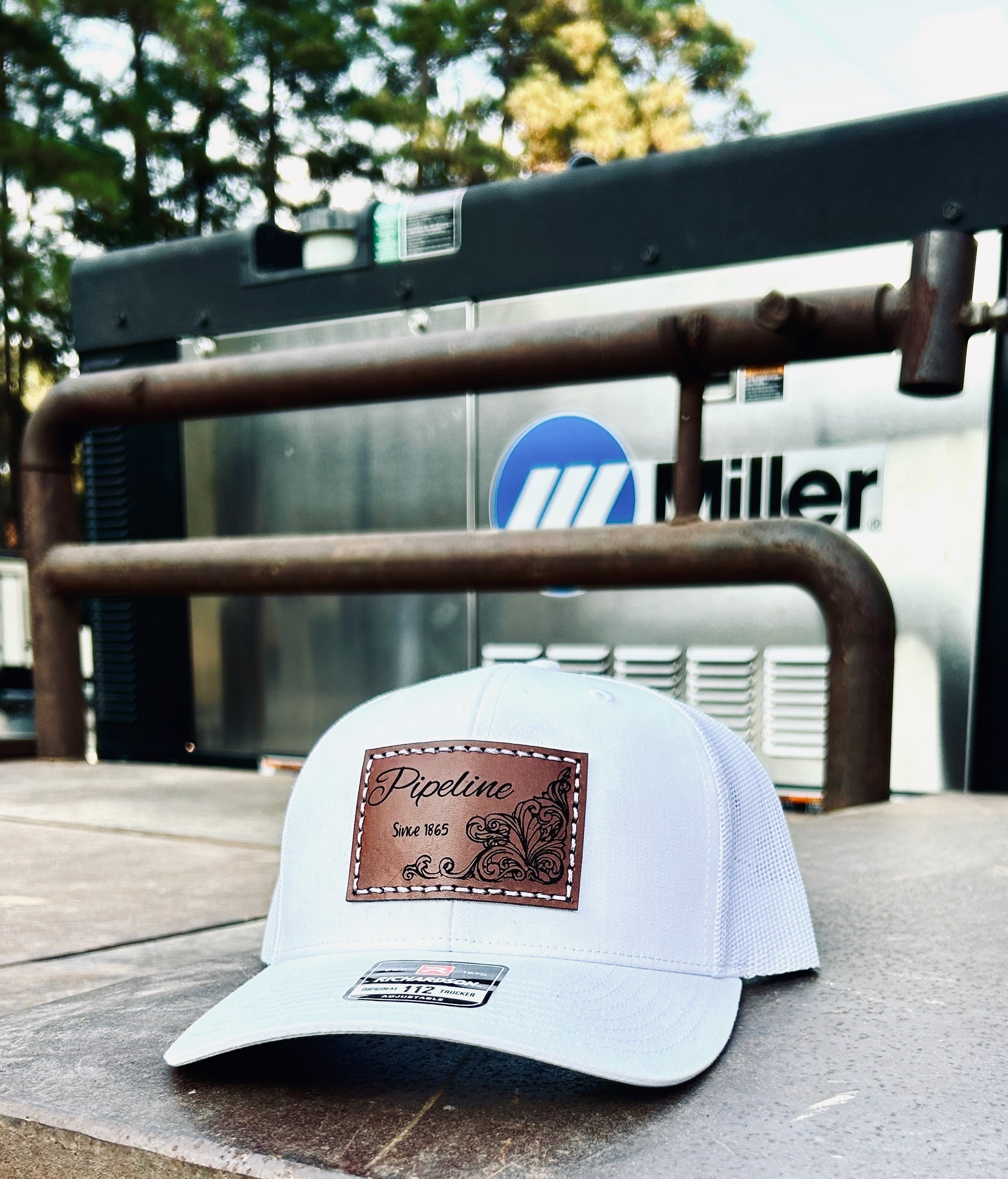 White cap with brown logo on a metal surface with 'Miller' branding in the background