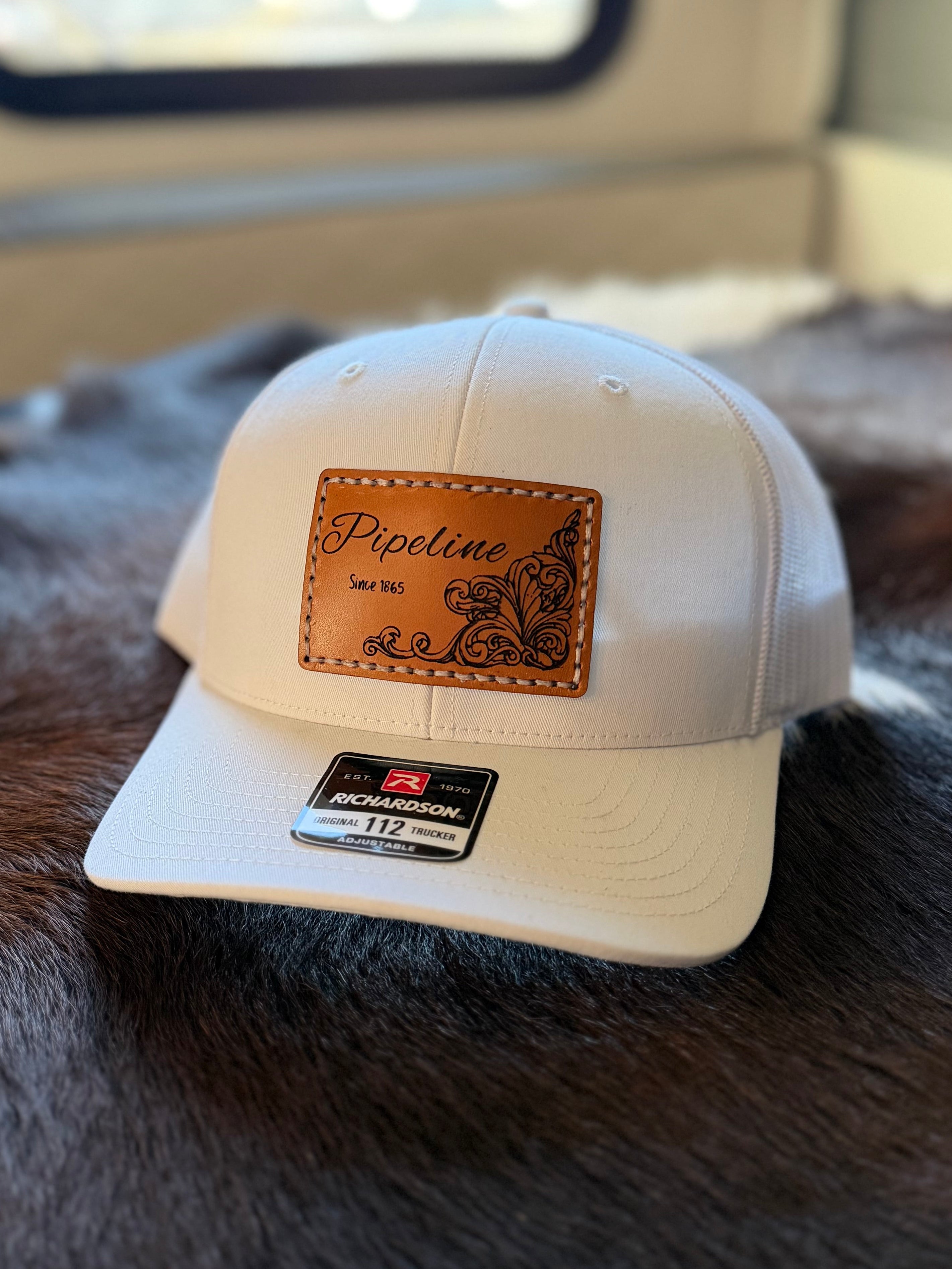 White cap with a brown leather patch on a textured cowhide surface, with a blurred background.