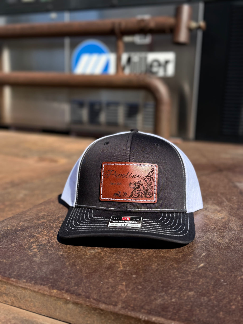 Black and white cap with leather patch on a wooden surface, with a blurred background featuring a truck.