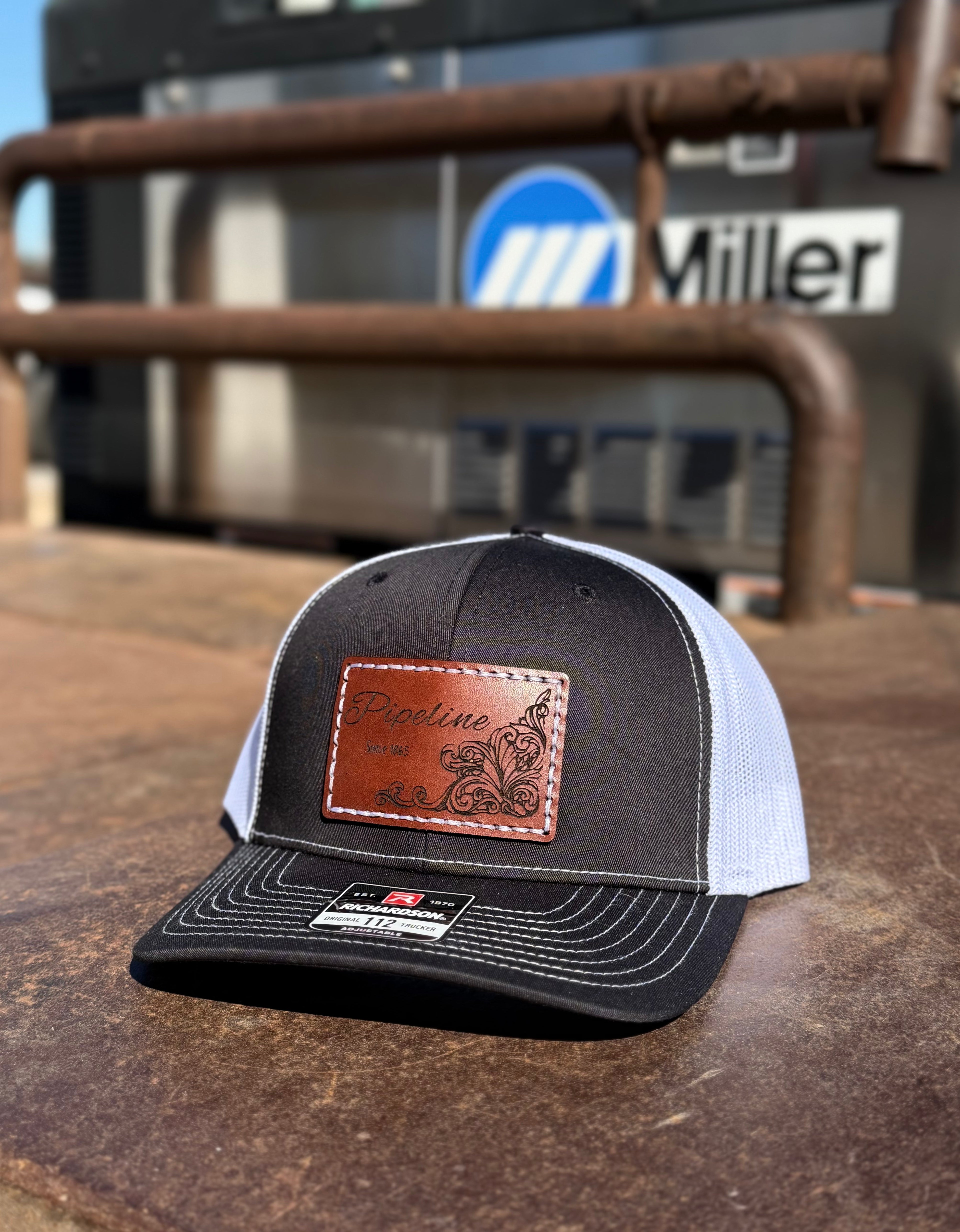 Black and white cap with a brown leather patch on a metal surface, with 'Miller' branding in the background.