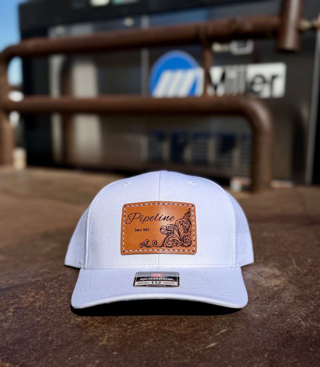 White cap with brown leather patch on a rustic surface with blurred background with a miller welder.
