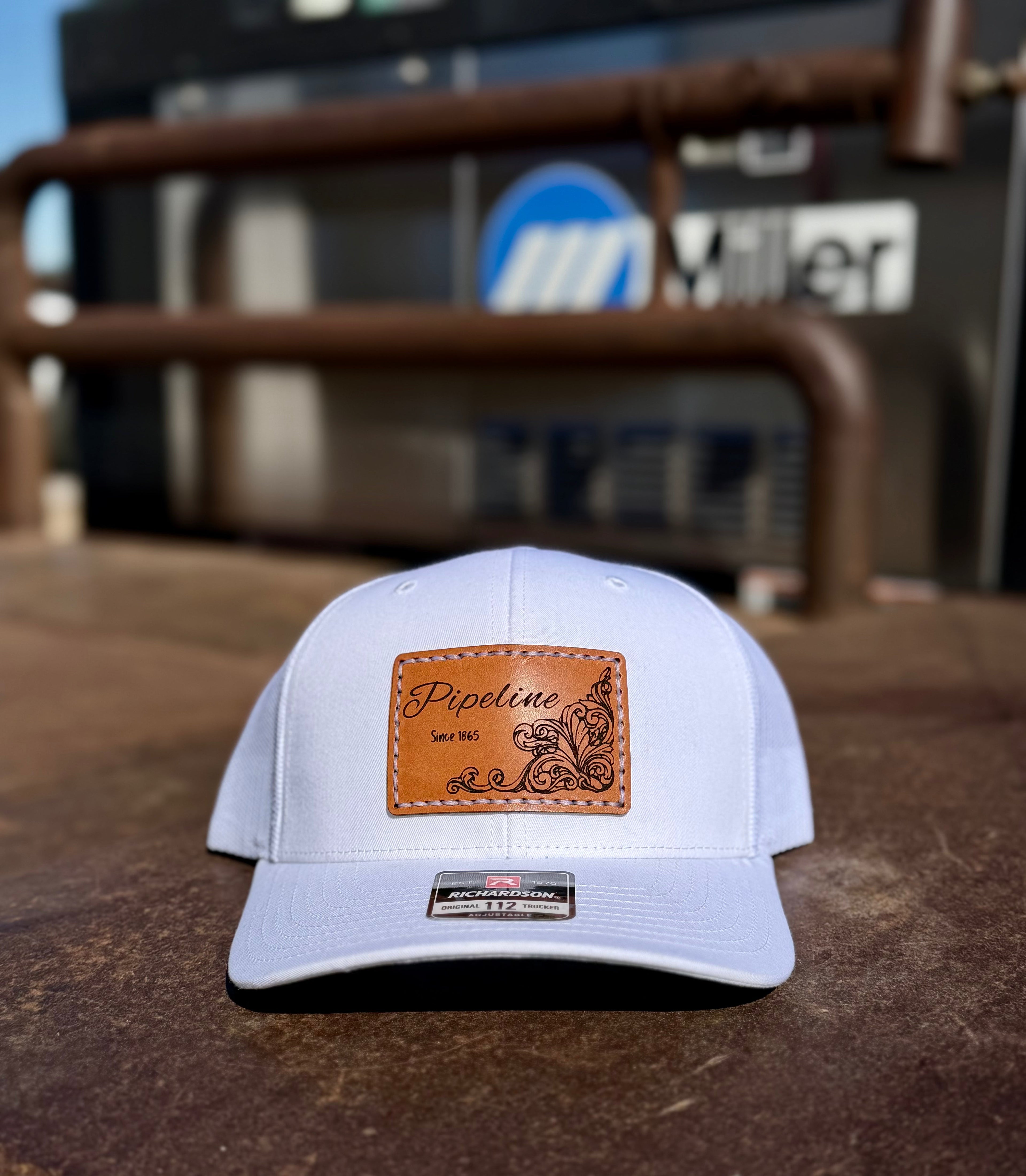 White cap with brown leather patch on a rustic surface with blurred background with a miller welder.
