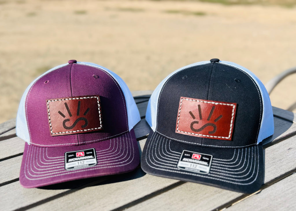 Two baseball caps with engraved leather patches on a wooden surface.
