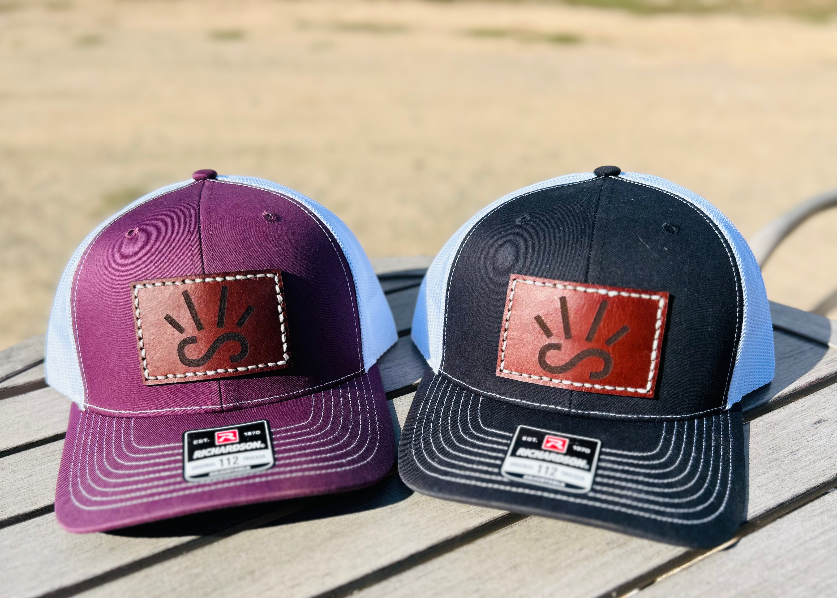 Two baseball caps with engraved leather patches on a wooden surface.