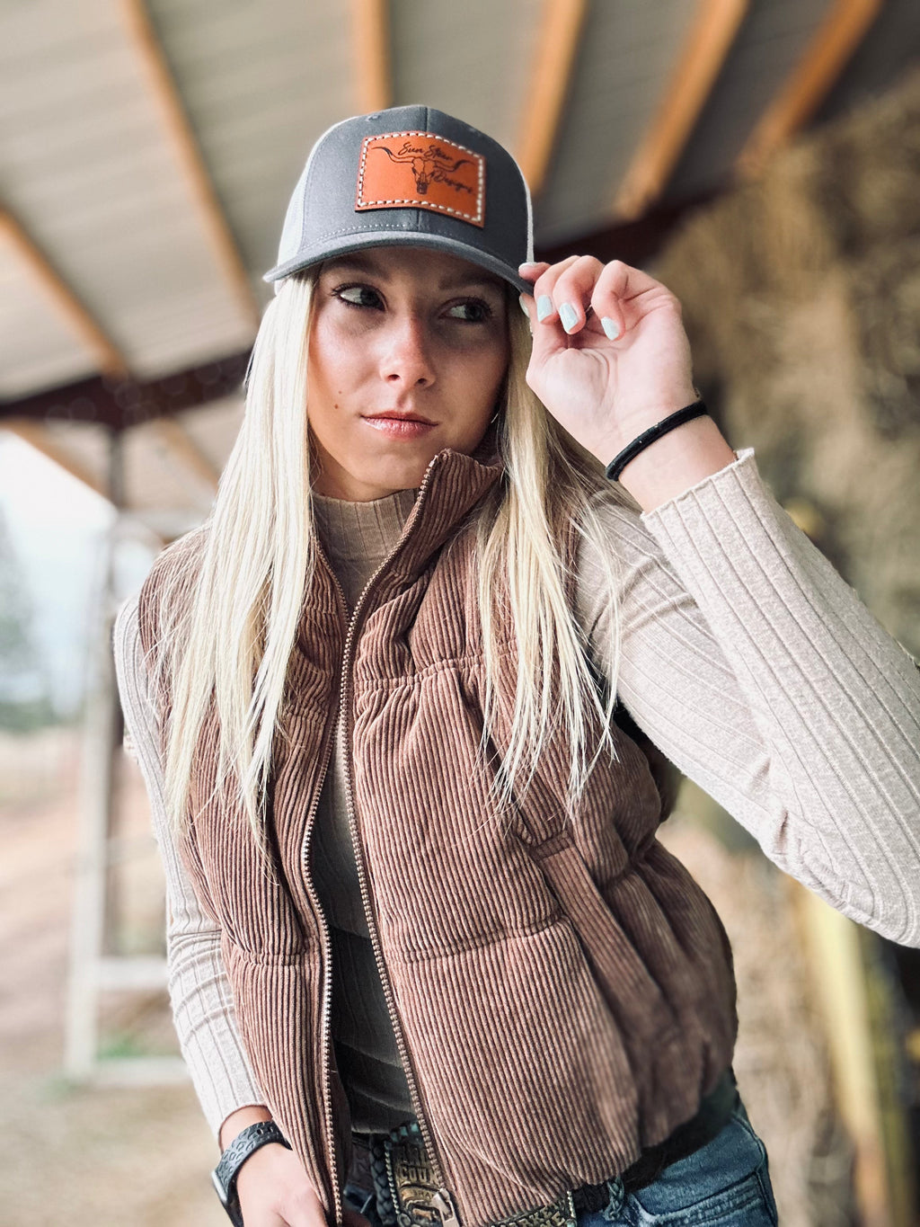 Person wearing a brown vest and cap with a leather patch, standing outdoors.