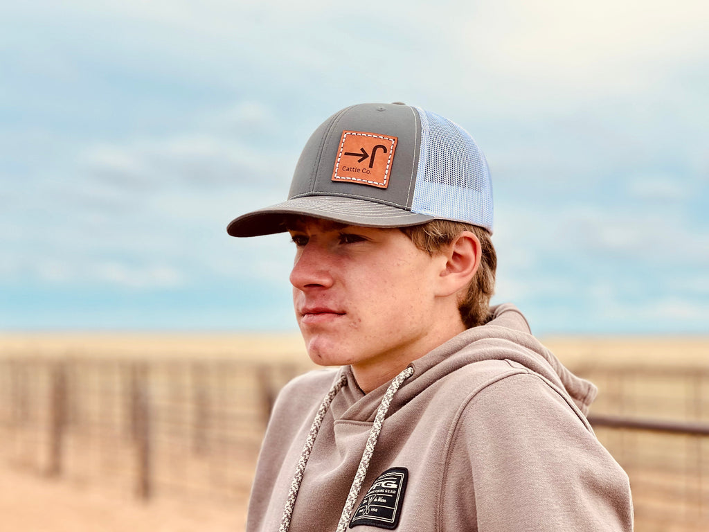 Person wearing a cap with a cattle brand on a leather patch and a hoodie in an outdoor setting
