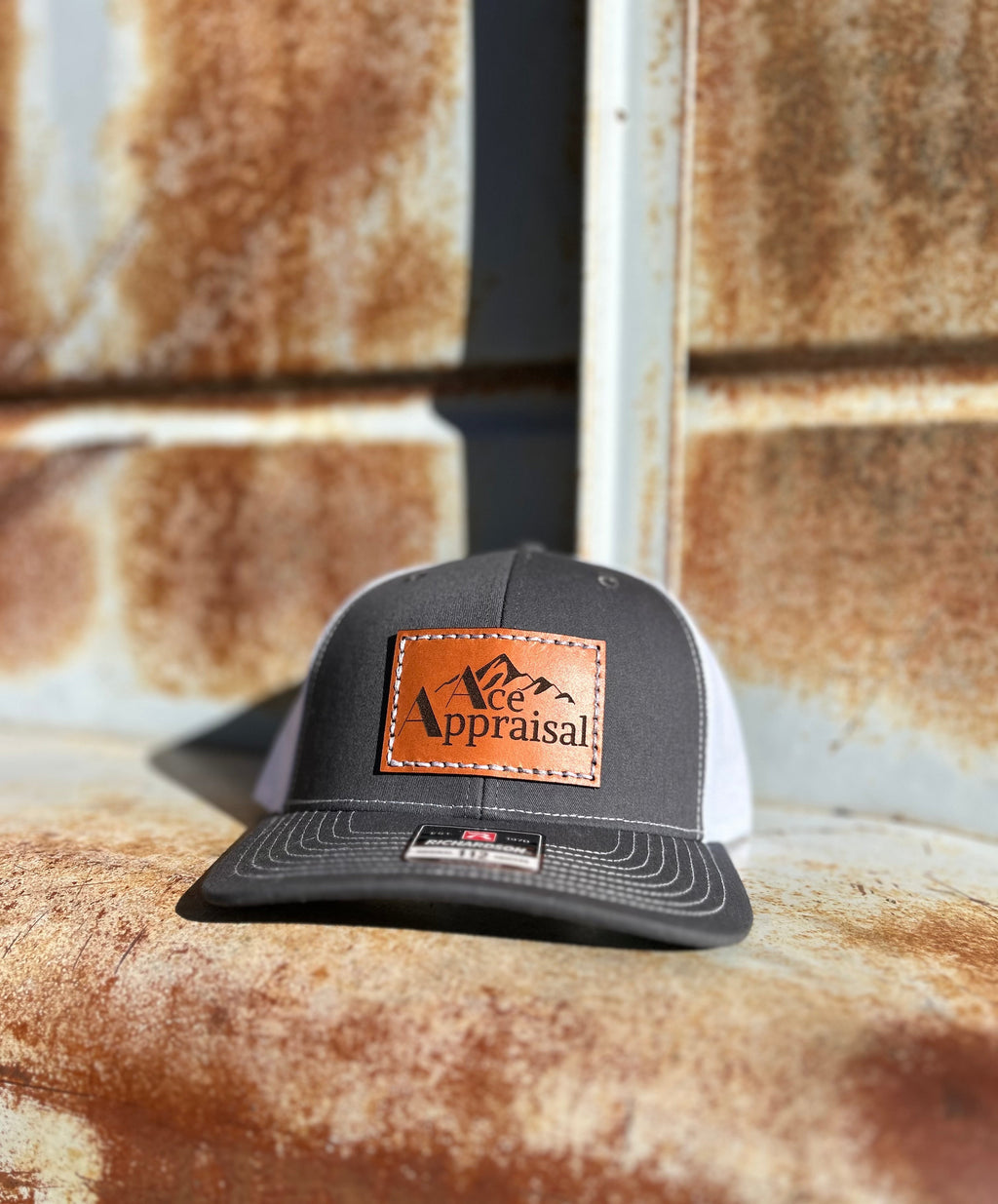 Grey and White Trucker hat with leather patch on a rusty metal surface