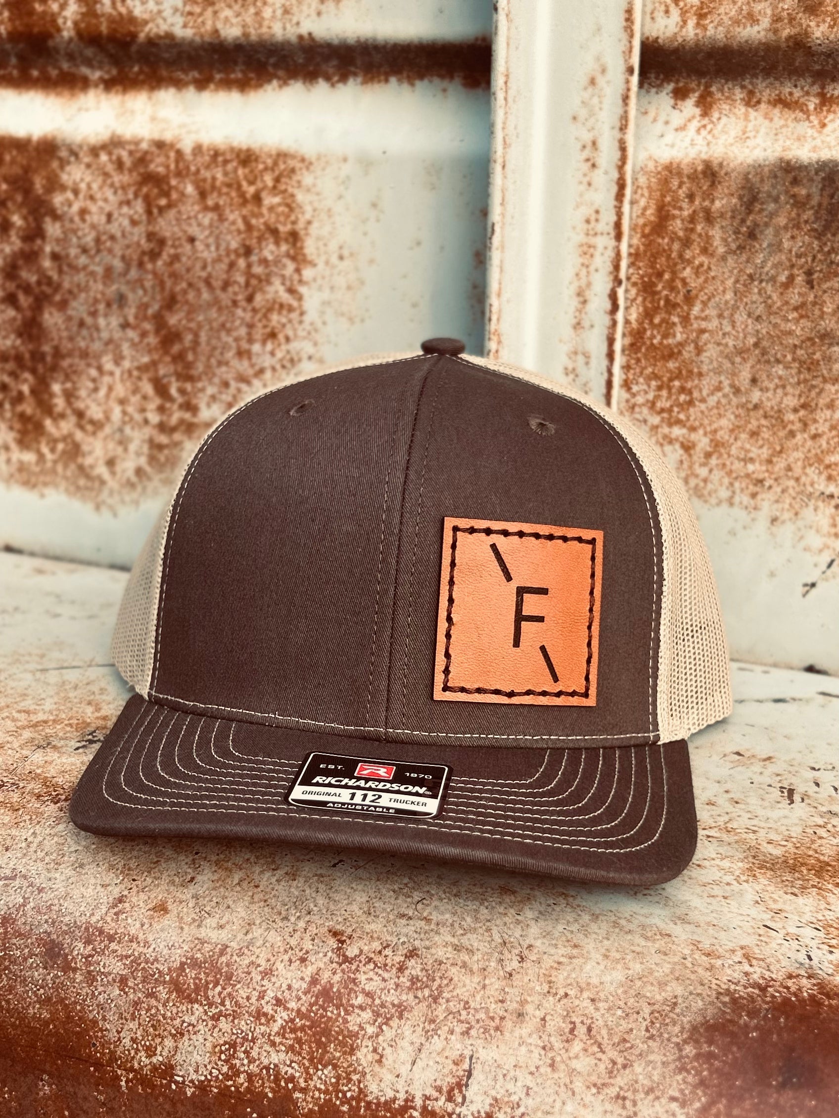 Brown trucker cap with leather patch on a rustic metal surface