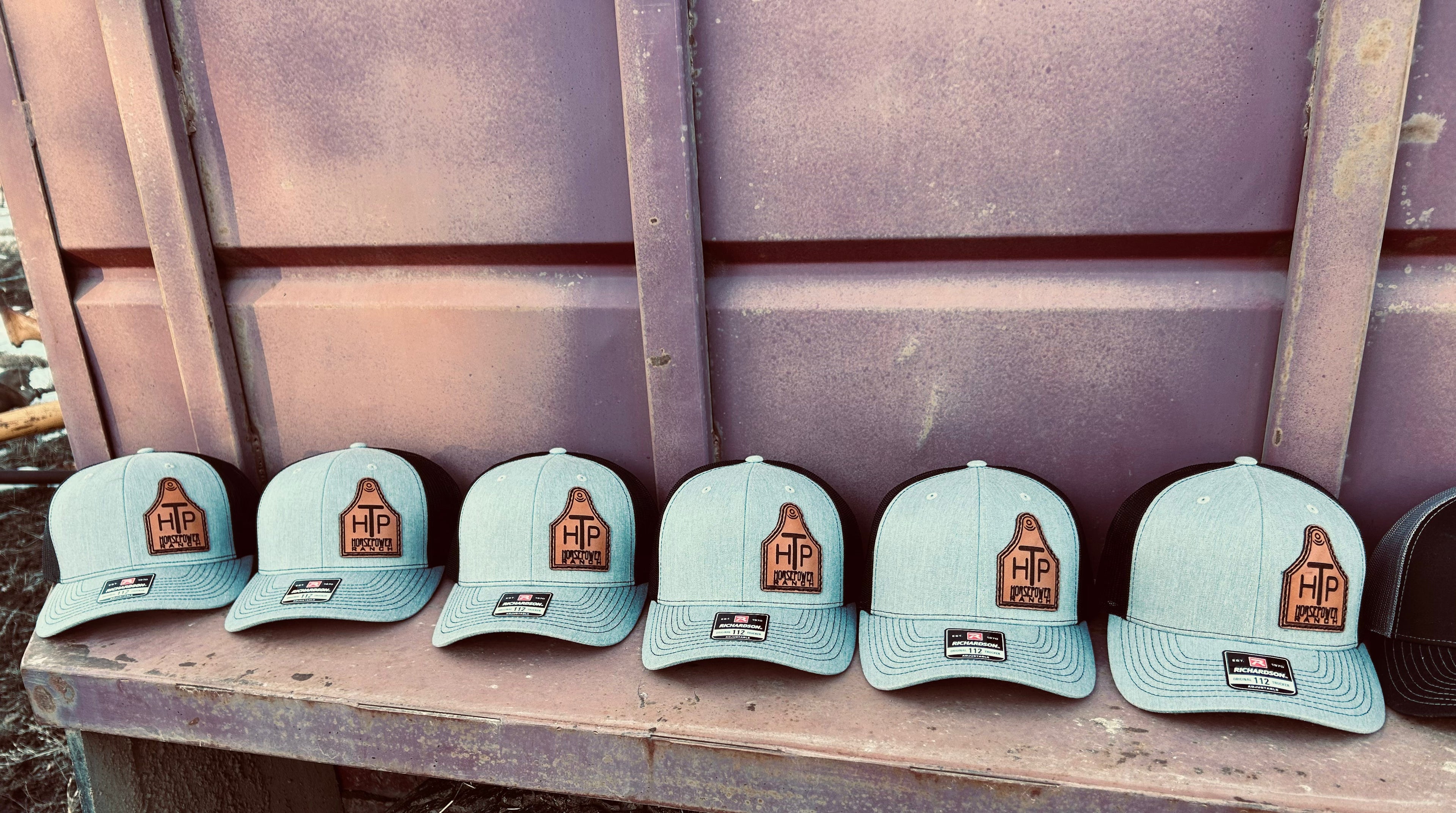 Six black and grey caps with a logo on a cowtag leather patch surface against a rustic background