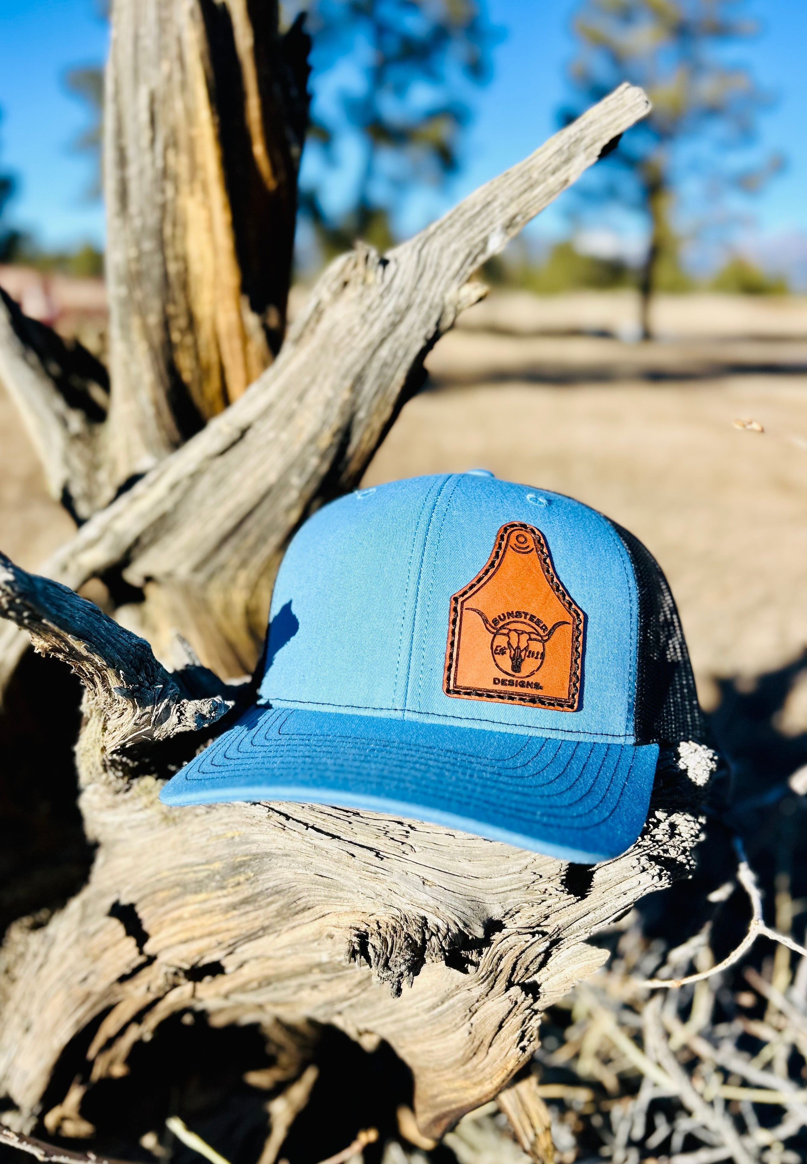 Blue trucker hat with a brown leather patch on a piece of driftwood.