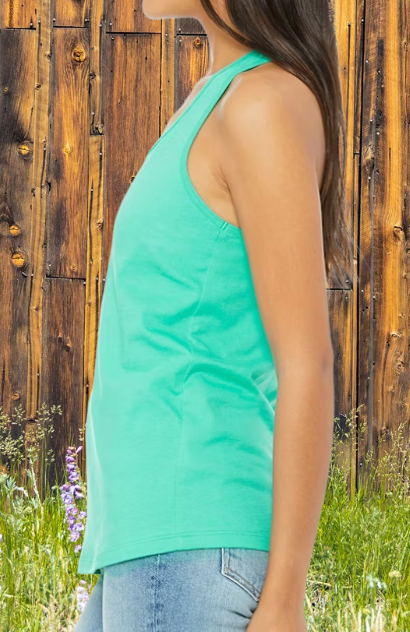 Person wearing a green tank top standing against a wooden fence with grass and flowers in the foreground.