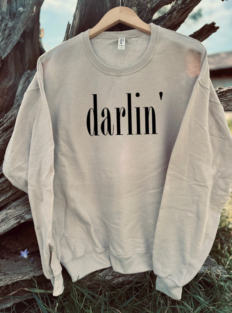 Sandstone tan sweatshirt with black 'darlin' text on a wooden hanger against a natural background
