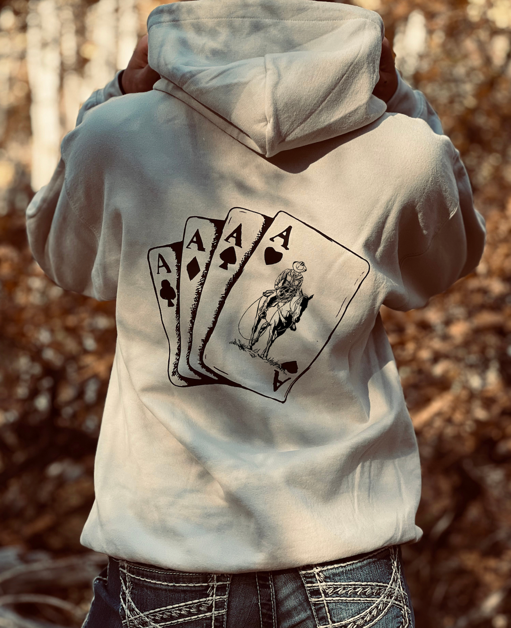Person wearing a hoodie with a graphic design on the back, standing in a natural setting.