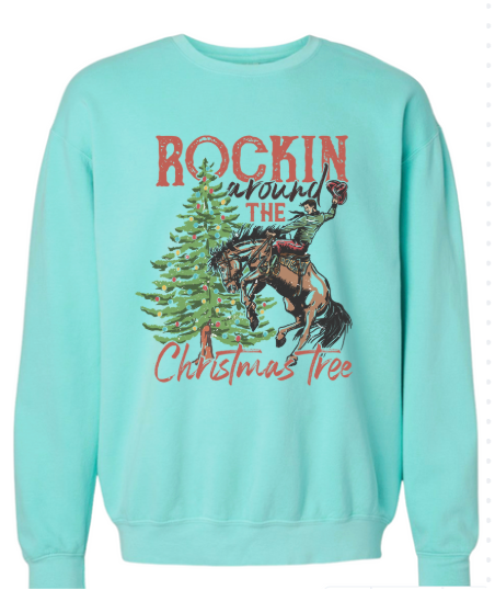 Light blue sweatshirt with a graphic of a person riding a horse around a Christmas tree and text 'Rockin' around the Christmas tree'.