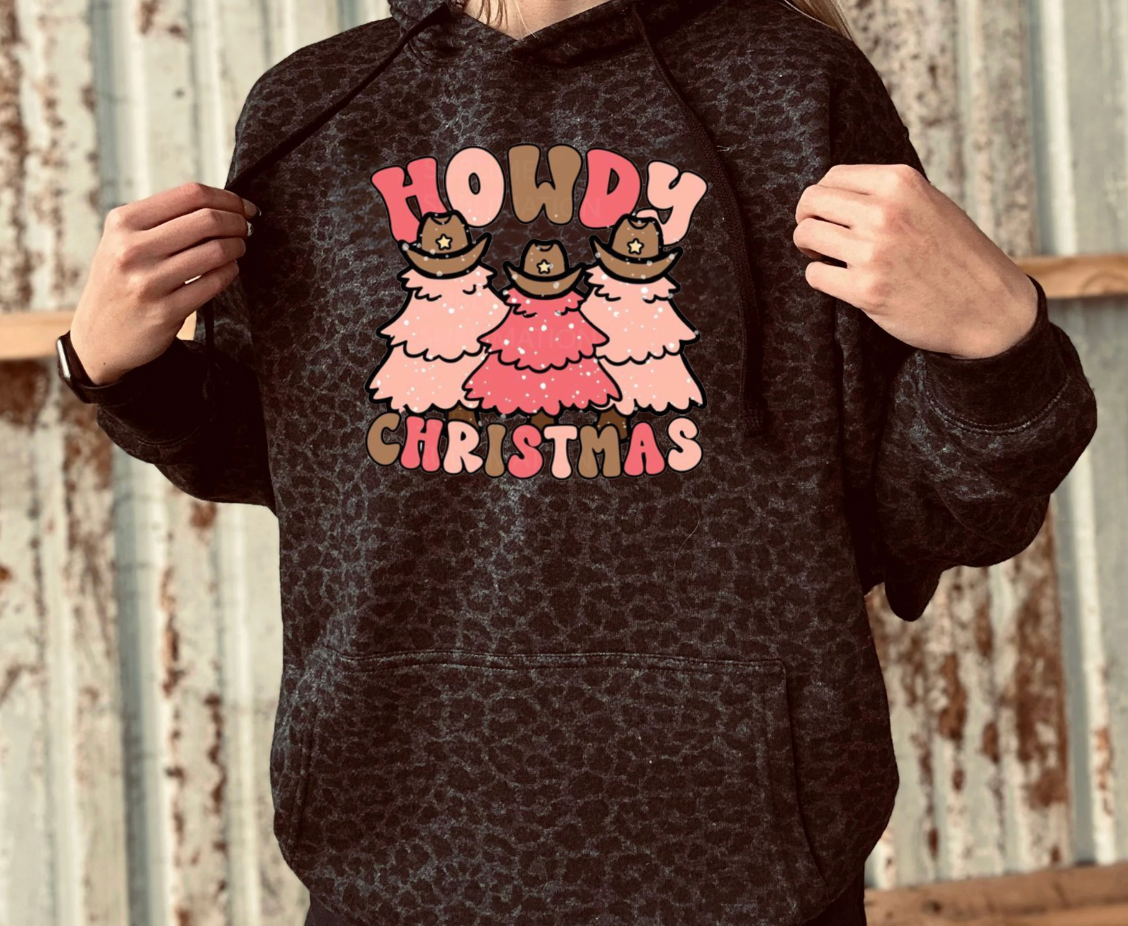 Person wearing a black leopard hoodie with 'Howdy Christmas' design against a rustic wooden background