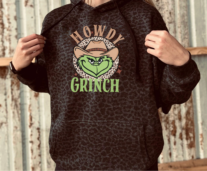 Black Leopard Hoodie with 'Howdy Grinch' graphic design against a wooden background