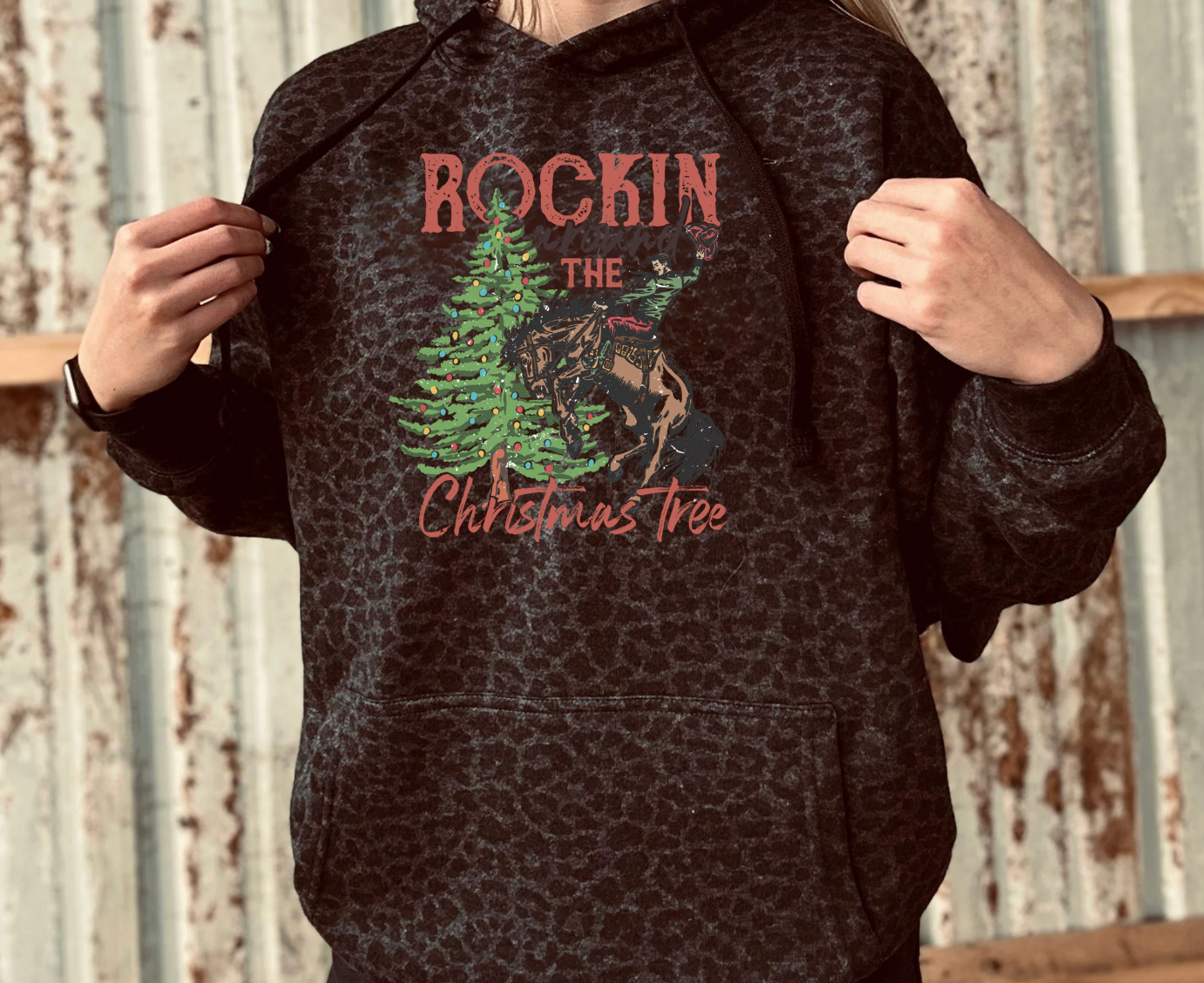 Person wearing a black leopard hoodie with a graphic design of a deer and Christmas tree, text 'Rockin the Christmas Tree'.