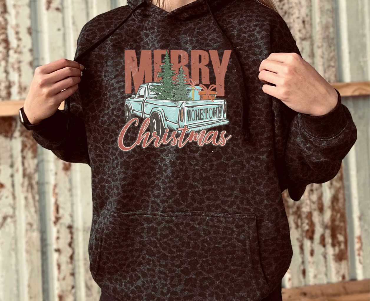Person wearing a black leopard print hoodie with a Christmas design featuring a truck and trees.