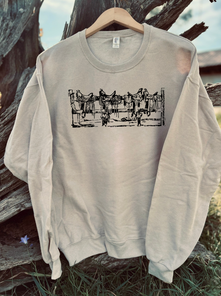 Sandstone sweatshirt with saddles on a fence black graphic design hanging on a wooden hanger against a natural background.