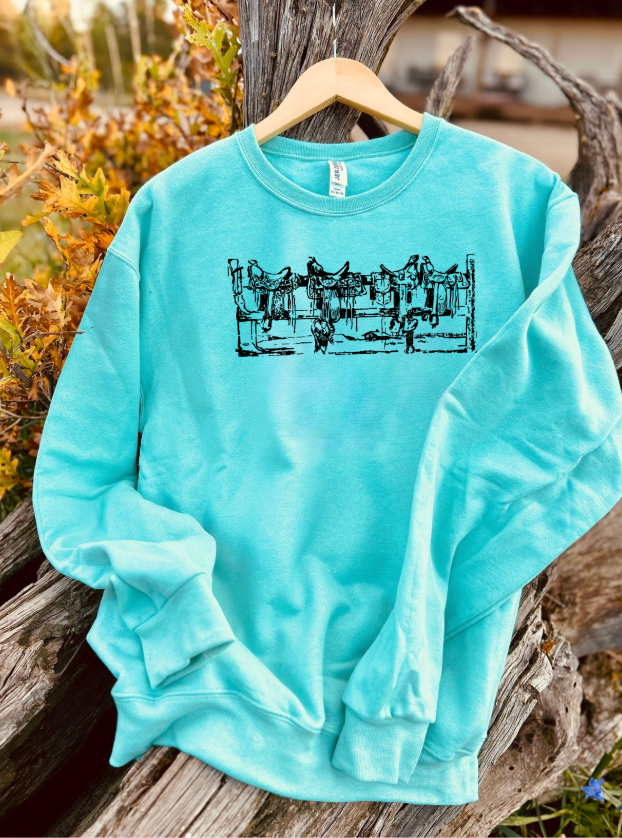 Mint sweatshirt with a black saddles on a fence graphic on a wooden surface with natural background