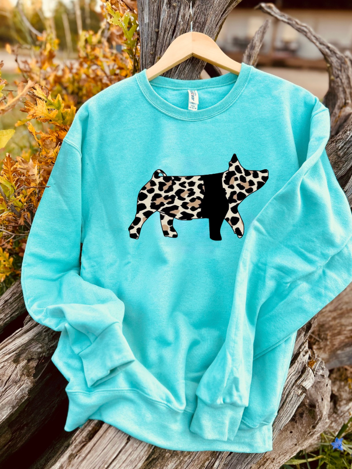 Turquoise sweatshirt with a leopard print pig design on a wooden surface with natural background