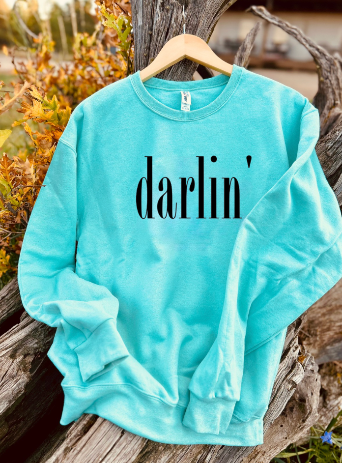 Turquoise sweatshirt with 'darlin' text on a wooden surface with natural background