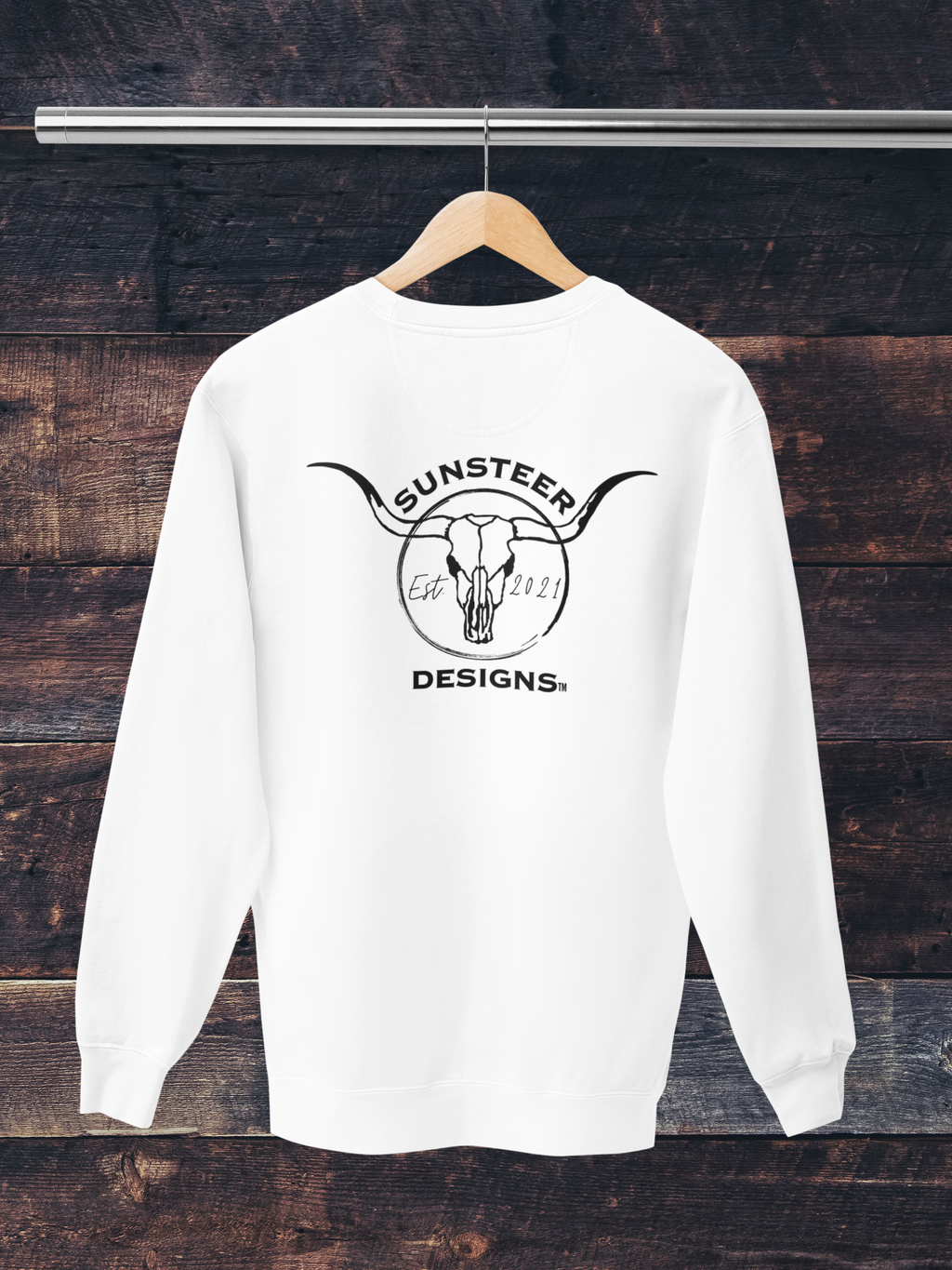 White sweatshirt with 'Sunsteer Designs' logo on a wooden background