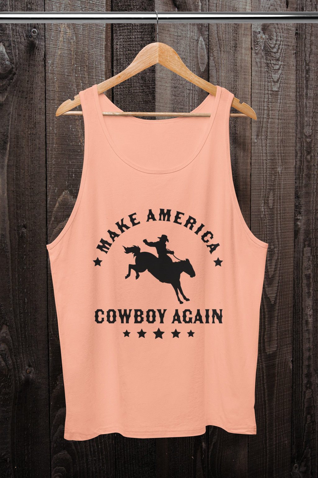 Pink tank top with 'Make America Cowboy Again' graphic on a wooden hanger against a wooden background