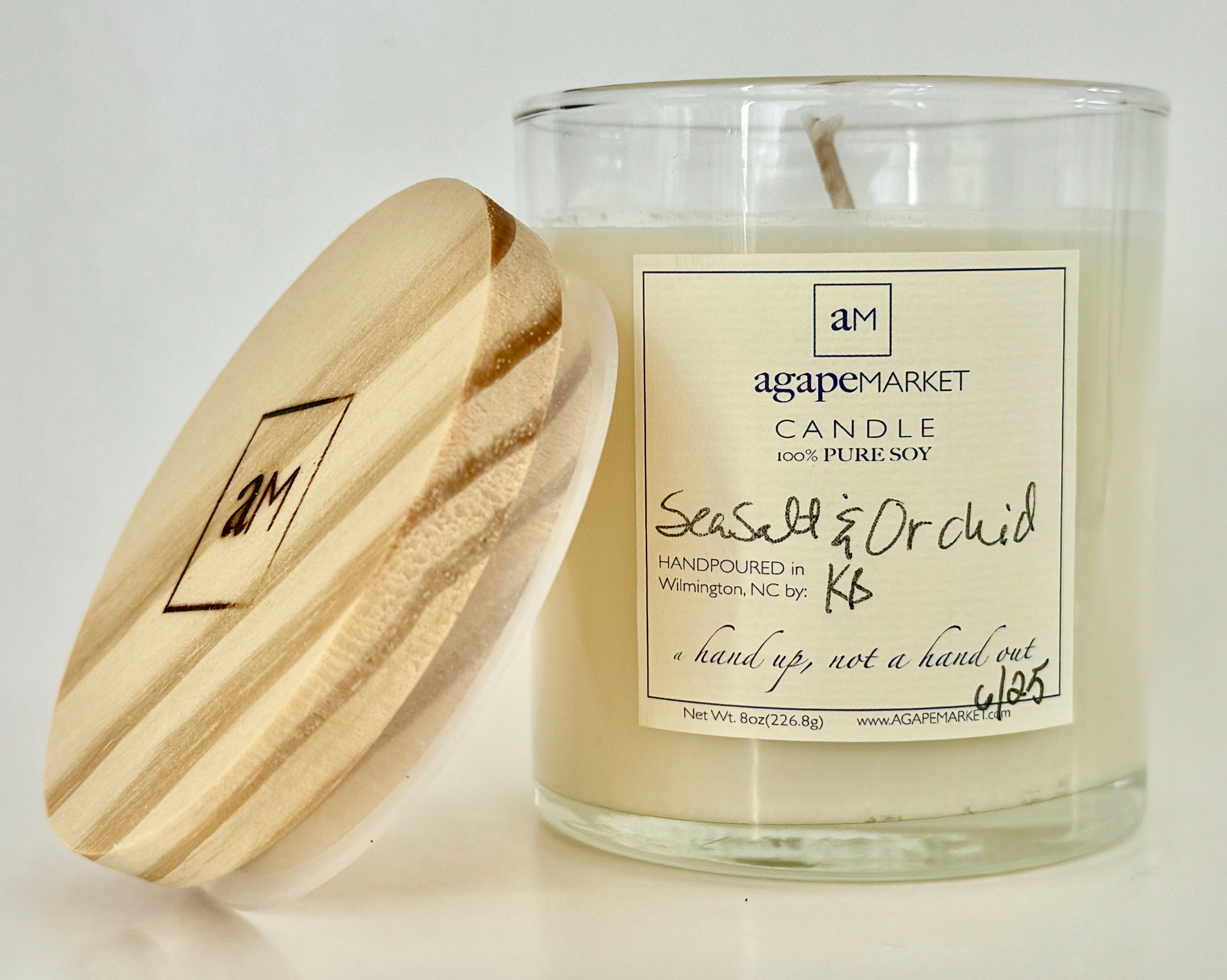 Soy candle in 8oz clear glass jar with white wax and a pine wood lid with logo leaning against the candle jar.
