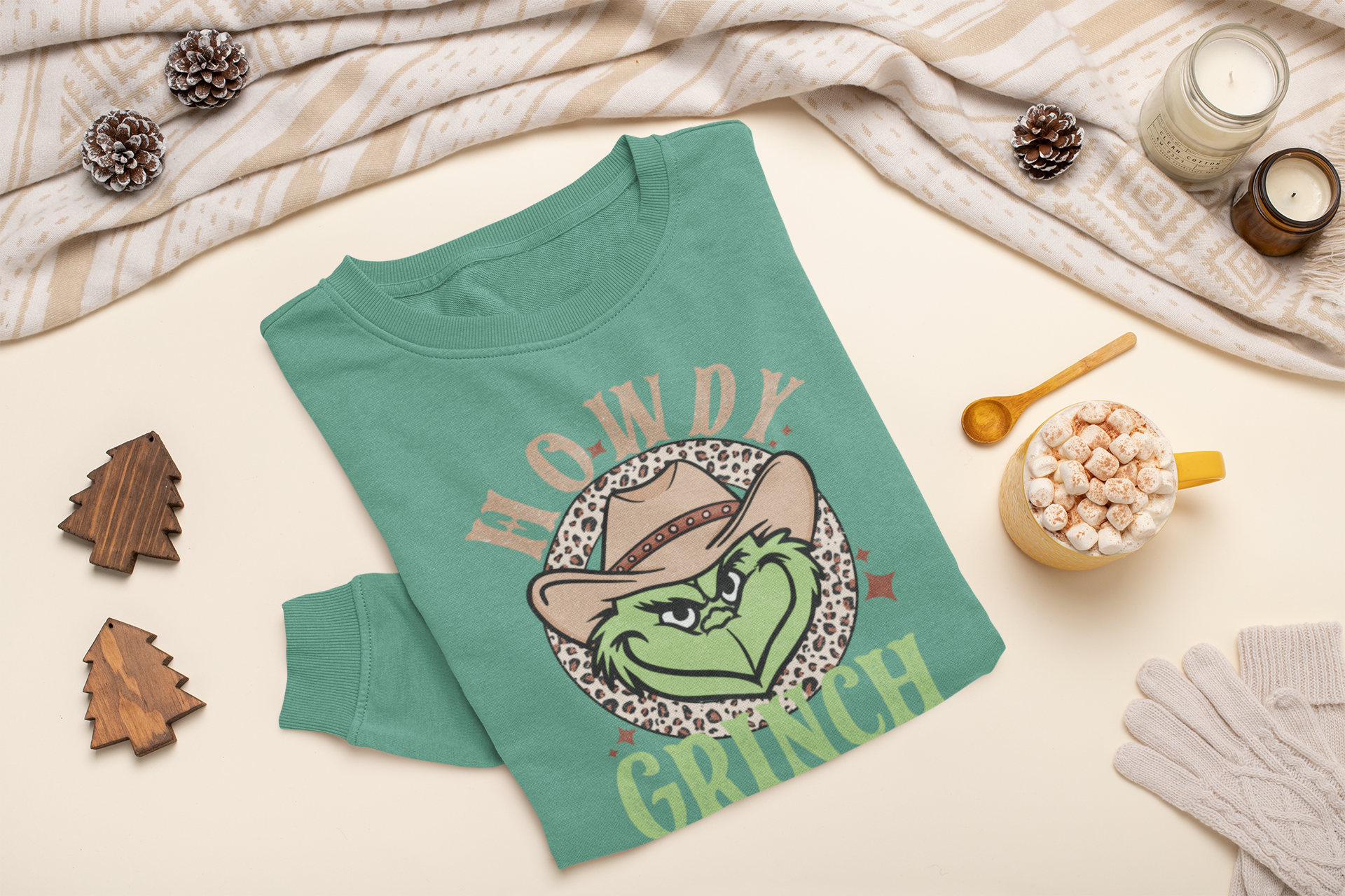Green sweatshirt with 'Howdy Grinch' design on a light surface with decorative items.