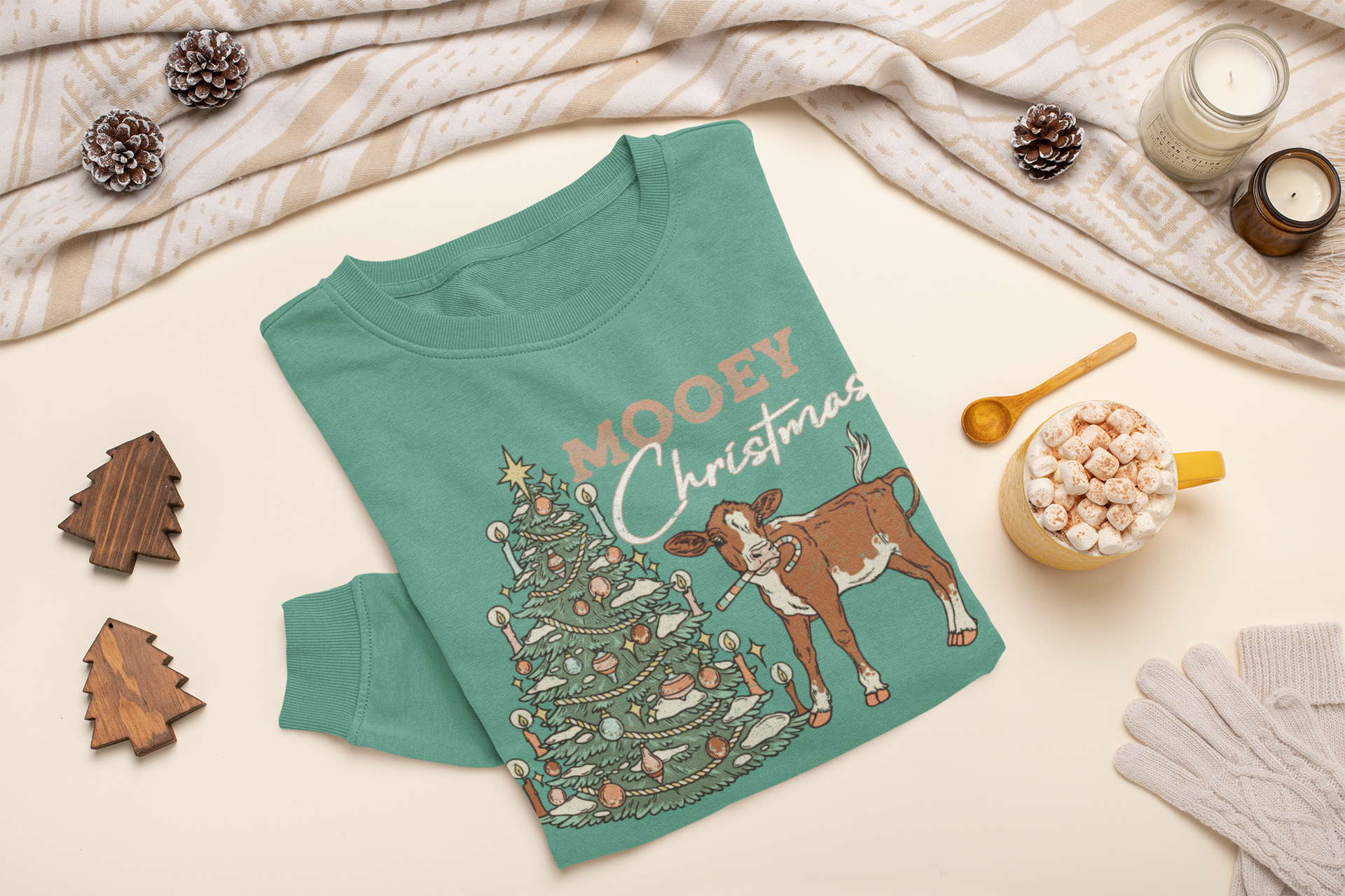 Green sweatshirt with Christmas design featuring a cow and tree, placed on a light surface with holiday decor.