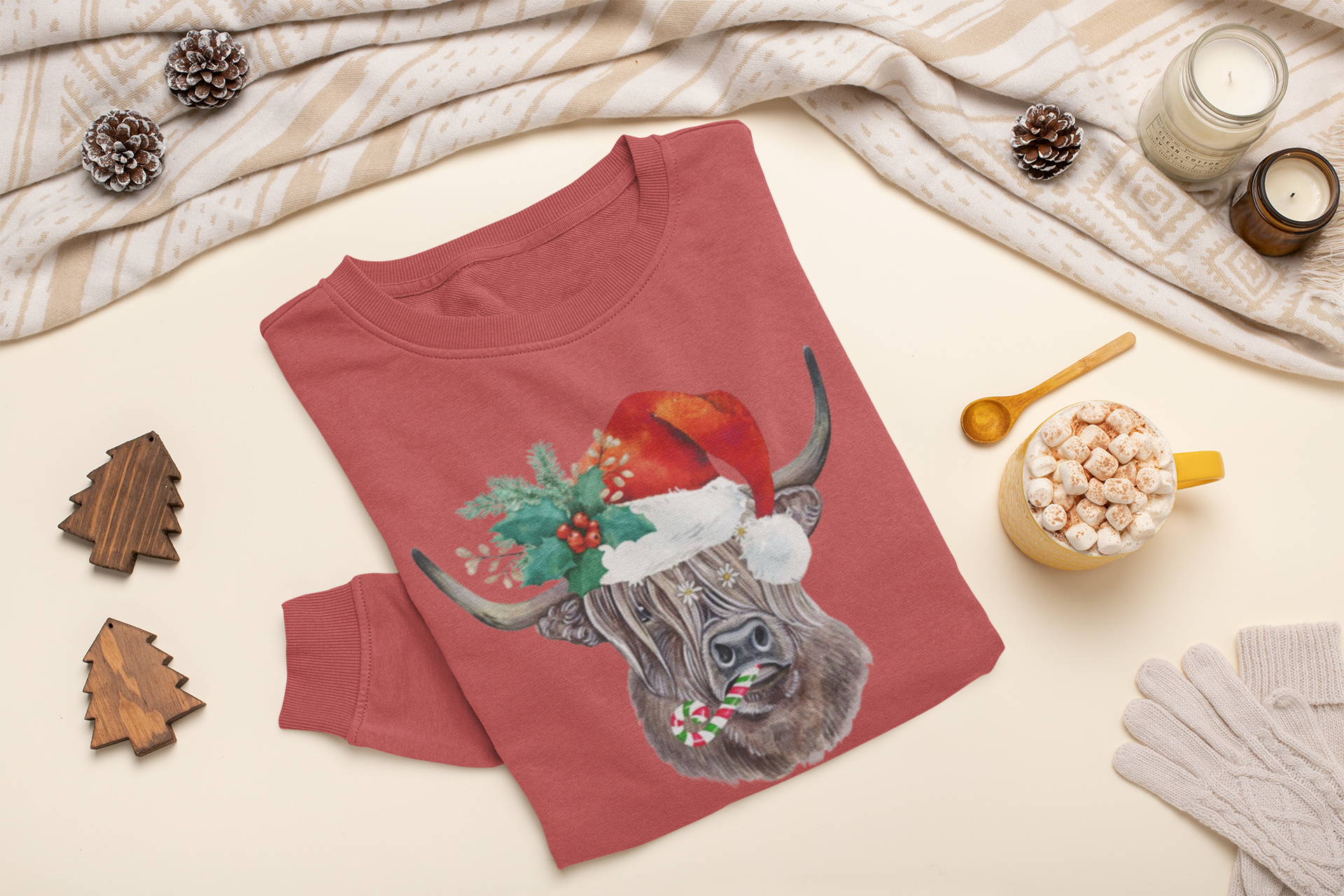 Red sweatshirt with a highland cow wearing a Santa hat on a beige surface with holiday decorations.