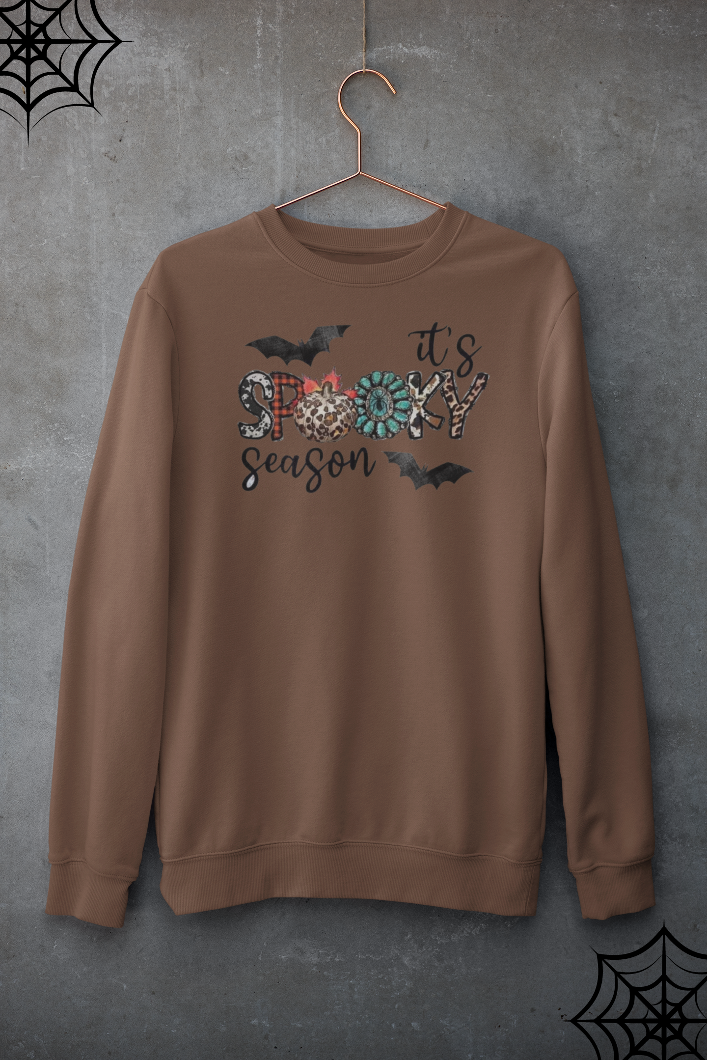 Brown sweatshirt with 'it's spooky season' text and bats on a gray background